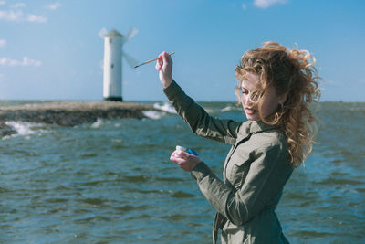 Side view of woman standing in sea against sky and painting 