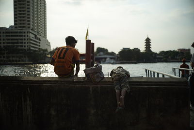 Rear view of man standing on river against buildings