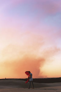 Woman standing on beach against sky during sunset