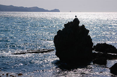 Silhouette rock on beach against clear sky