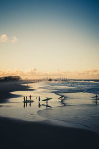 Surfers at beach against sky during sunset