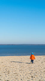 Rear view full length of boy walking at beach against clear blue sky