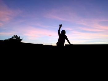 Silhouette boy on rooftop against sky during sunset