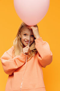 Portrait of young woman with balloons against yellow background