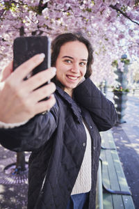 Young woman taking selfie against cherry trees