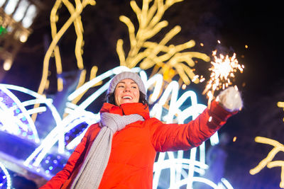 Portrait of woman standing against illuminated christmas