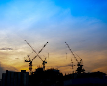 Low angle view of silhouette cranes against buildings at sunset