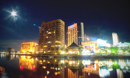 Illuminated city by river against sky at night