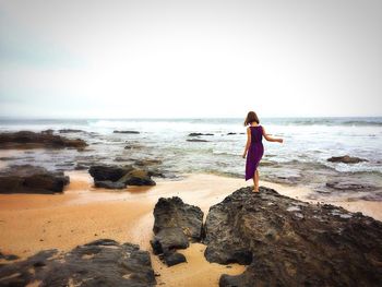 Rear view of woman standing on beach against clear sky