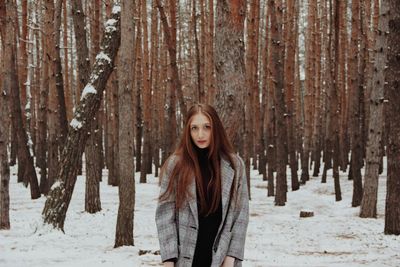 Portrait of young woman standing in snow covered forest