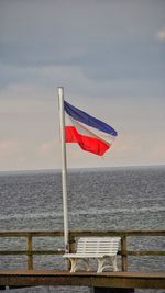 Red flag on railing by sea against sky