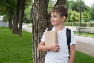 Boy standing by tree trunk against plants