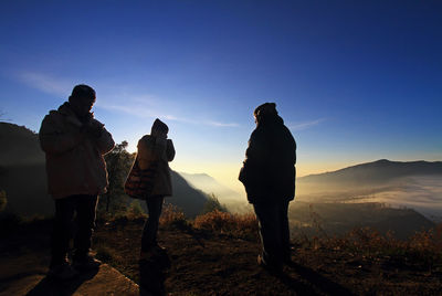 Rear view of people standing on mountain against sky