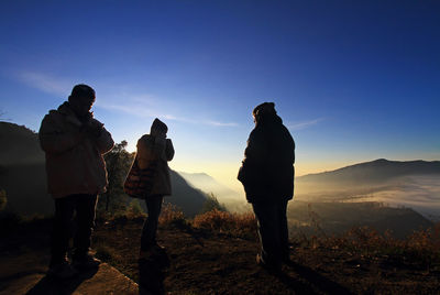 Silhouette people standing on top of mountain at sunset