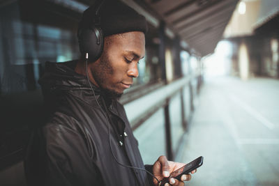 Man listening music on headphones while leaning on window