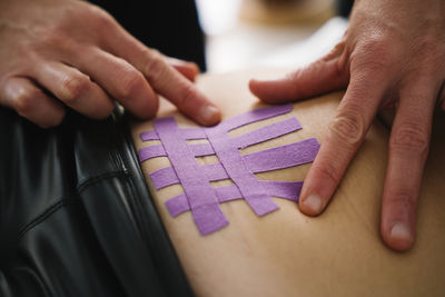 Female nurse applying purple elastic therapeutic tape on woman abdomen