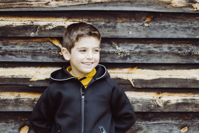 Smiling boy looking away against old wooden wall