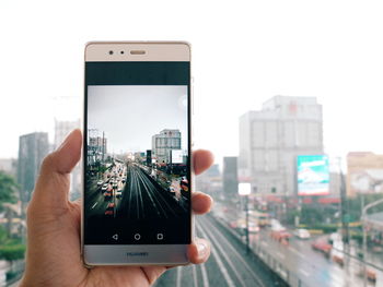 Close-up of hand photographing cityscape against sky