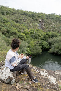 Woman drinking mate while relaxing sitting outdoors in nature.