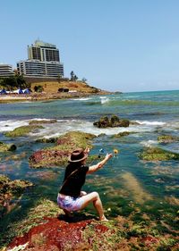 Man sitting at beach against clear sky