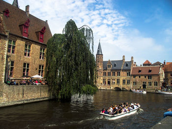 Boats in river by buildings against sky