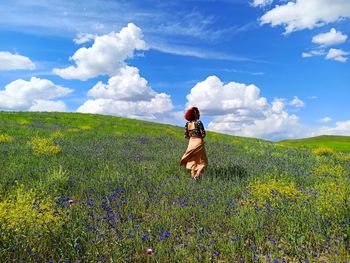 Rear view of woman standing on field against cloudy sky