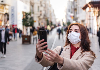 Woman wearing mask while using mobile phone while standing outdoors