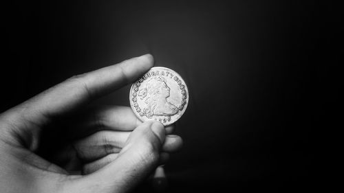 Close-up of hand holding coin against black background