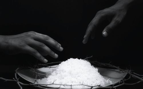 Cropped hands reaching towards rice amidst thorns in plate against black background