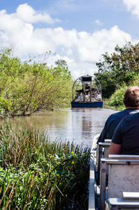 Rear view of man sitting by river against sky