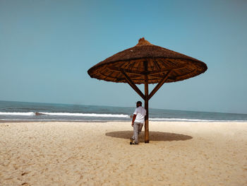 Rear view of man standing at beach against clear sky