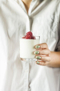 Midsection of woman holding yogurt and raspberries in drinking glass