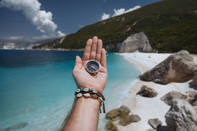 Midsection of person on rock at sea shore against sky