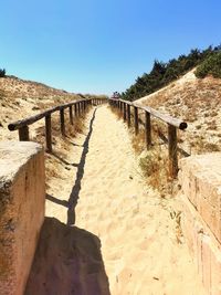 Footpath leading towards beach against clear blue sky