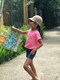 Side view of girl holding kite while standing on footpath