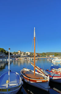 Sailboats moored in harbor against clear blue sky