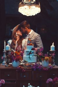 Newlywed couple kissing while standing by cake
