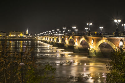 Illuminated bridge over river against sky in city at night