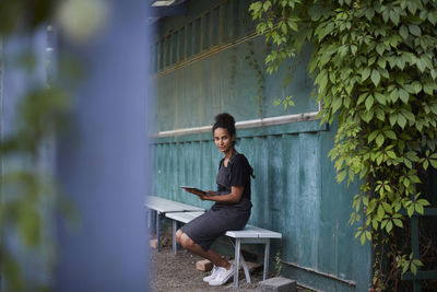 Portrait of female gardener holding digital tablet while sitting on bench