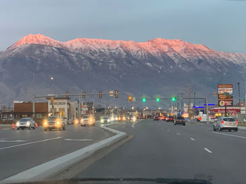 Cars on road by illuminated mountains against sky