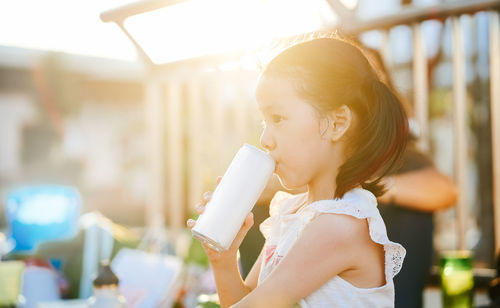 Side view of girl having drink in yard during sunset