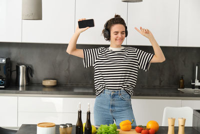 Full length of young woman with arms raised standing at home