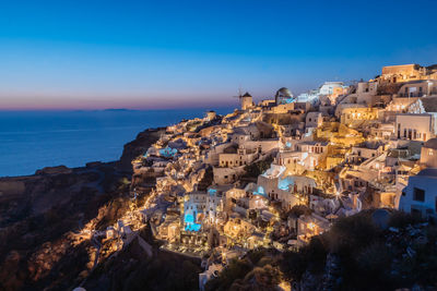 Aerial view of illuminated city by sea