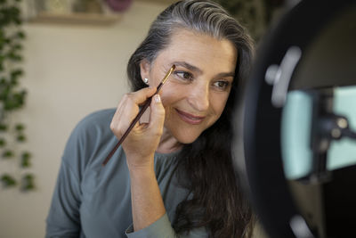 Smiling female vlogger brushing eyebrows during tutorial at home