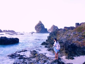 Rear view of woman standing on rock by sea against clear sky