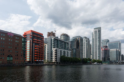 Modern buildings by river against sky in city