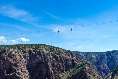 Low angle view of people on ski lifts over mountain against sky