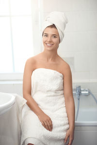 Portrait of smiling young woman sitting on bathtub at home