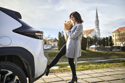 Woman carrying grocery bag opening car trunk with foot sensor