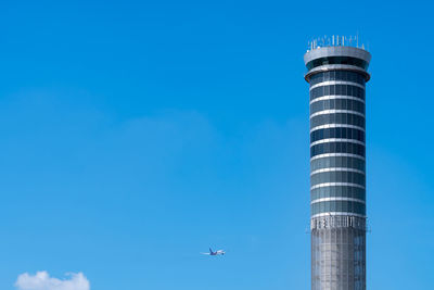 Air traffic control tower in the airport with international flight plane flying on clear blue sky.
